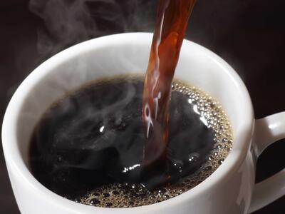 Sort, vellavet kaffe skænkes op i hvid kaffekop.