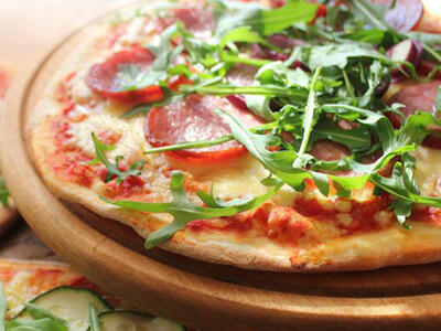 Hjemmelavet pizza med rucola, pepperoni, ost og tomat på spækbræt af træ.