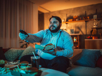 Man sidder med en fjernbetjening og noget mad