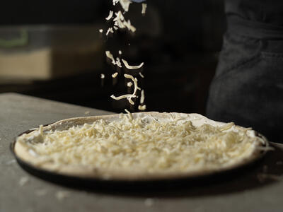 Person fordeler pizzatopping på en pizzabund
