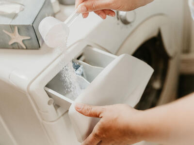 Person hælder vaskepulver i vaskemaskinen