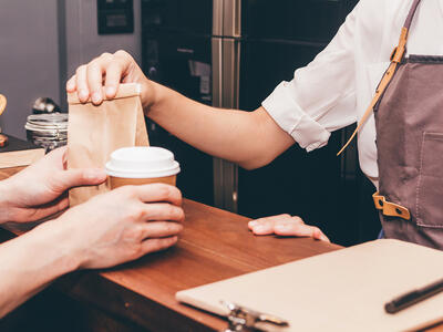 En medarbejder på en cafe betjener en kunde og sælger ham en kaffe og noget sødt til 