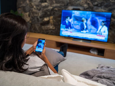 Kvinde sidder med sin telefon imens hun ser tv