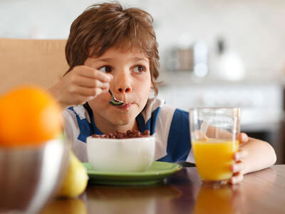 Barn spiser morgenmad fra skål med en ske. Morgenmadsprodukter er ikke nødvendigvis så sunde, som pakkerne antyder. 