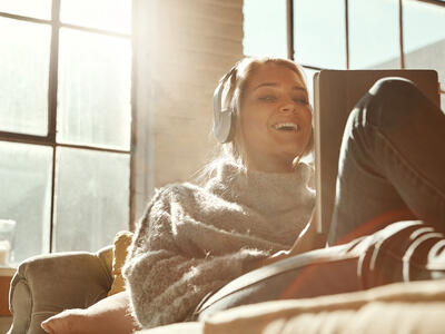 Kvinde sidder i en sofa og kigger på en skærm med høretelefoner på