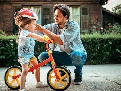 Pige sidder på løbecykel mens far giver hende cykelhjelm på