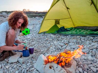 Kvinde laver instant kaffe på telttur over bål.