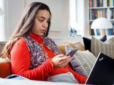 Kvinde med telefon og computer ser overrasket ud