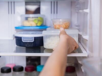 hånd rækker ind i køleskab med madrester i forskellige plastikbøtter