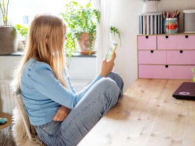 Teenagepige sidder på værelse og kigger på smartphone