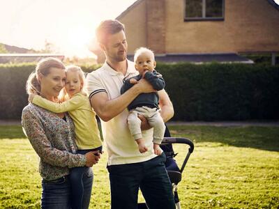 Kvinde og mand med to børn står i haven og kigger på deres nye hus