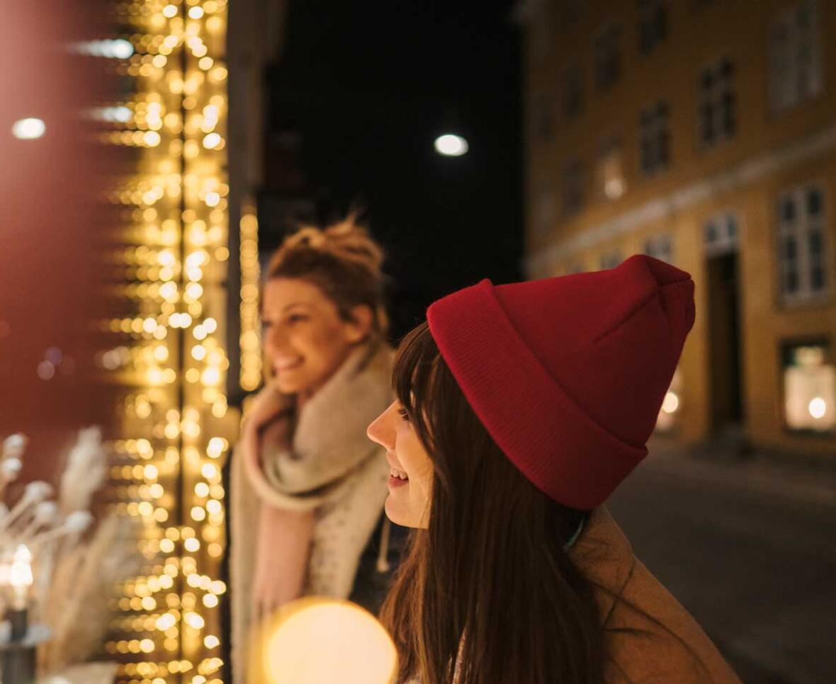 To kvinder kigger på butiksvindue lyst op med julelys