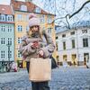 Person i vintertøj står med papirspose i den ene hånd og smartphone i den anden hånd, i København